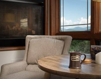 Brown fabric chair with a table and Lucille's Coffee mug with a window and a Mountain view